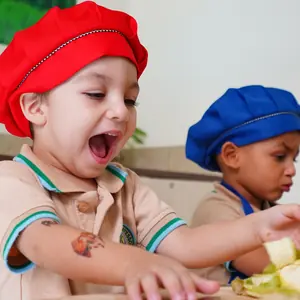 Two children in chef hats laughing while preparing fruit