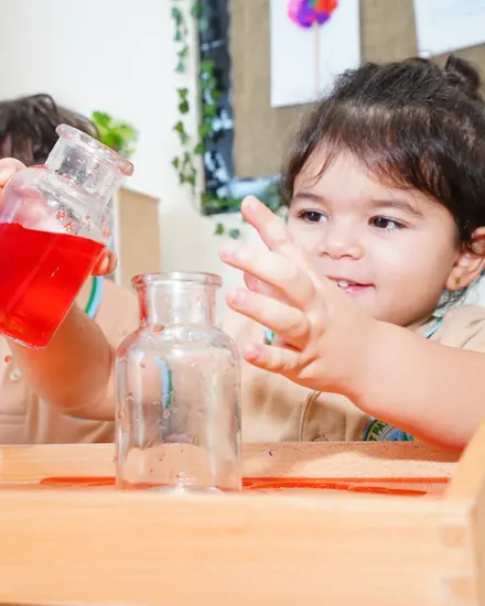 A child pouring coloured water between glass jars at a Montessori practical-life table