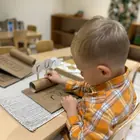 A child writing letters on a card at a school-readiness table