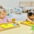 Two toddlers pressing shapes into yellow dough on wooden trays