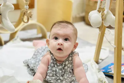 An infant on a soft play mat under a wooden play gym in the Pines room